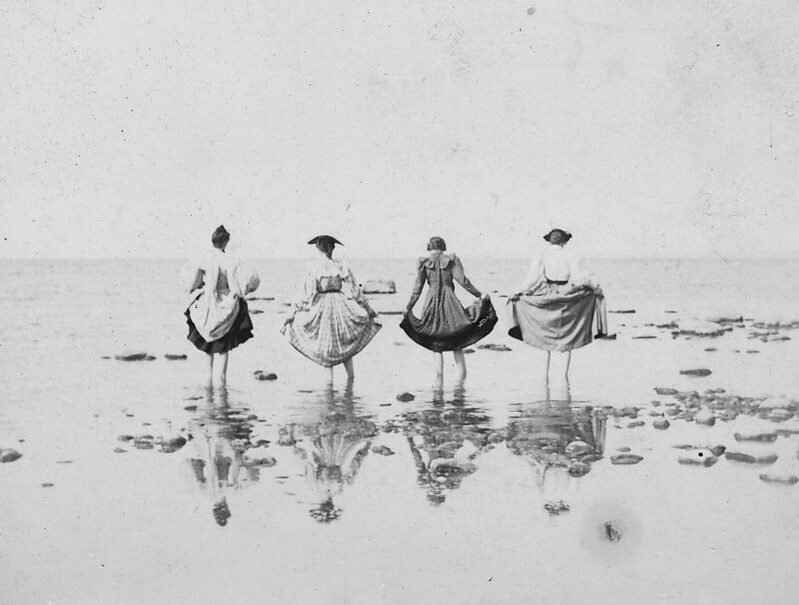 Black and white photograph of the waders in the bay, showing four females lifting their skirts and wading in a rocky area, 1901.; Images and documents may be protected by copyright law. Contact Traverse Area District Library for permission to reproduce, display, or transmit this image.; S. E. Wait Album; S.E. Wait?, “The waders in the bay, showing four females lifting their skirts and wading in a rock area, 1901.,” TADL Local History Collection, accessed October 15, 2025, https://localhistory.tadl.org/items/show/22075.