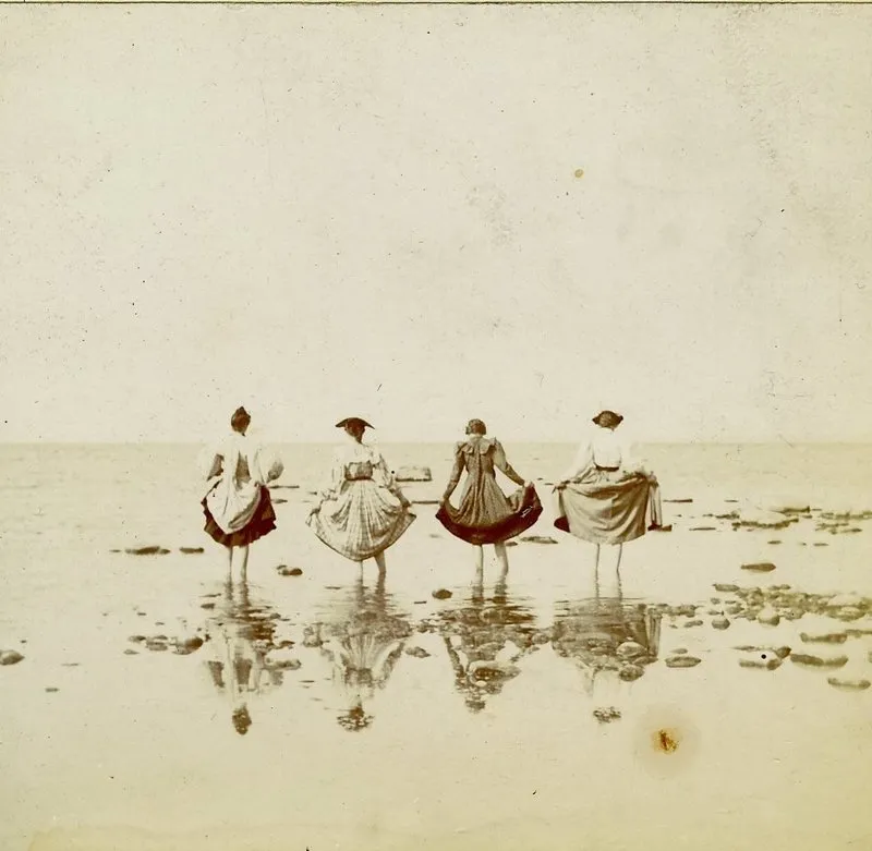 Ladies in the shoreline lifting their skirts above their ankles